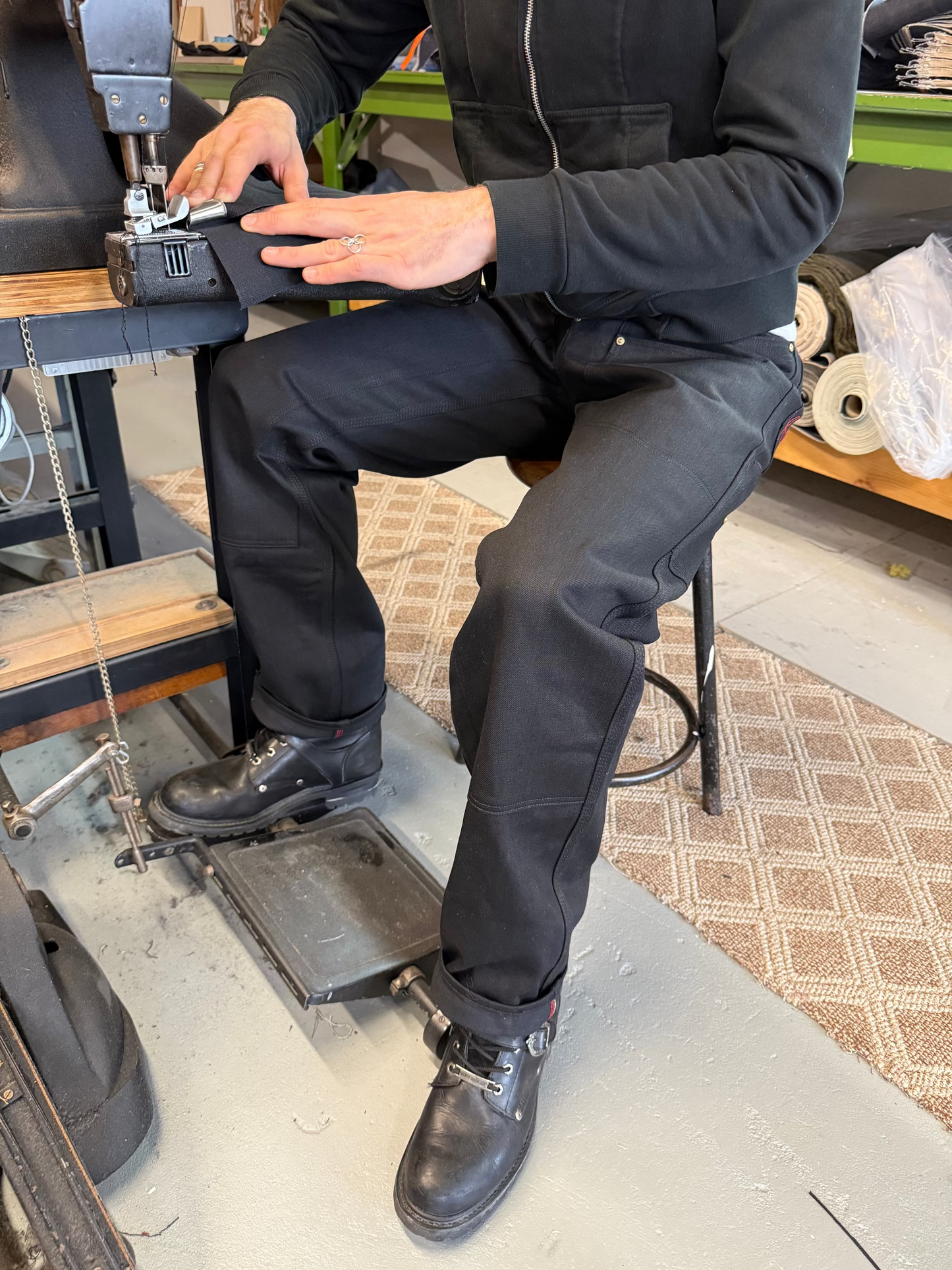Person operating a sewing machine in a workshop setting wearing the Black triple front workwear jeans