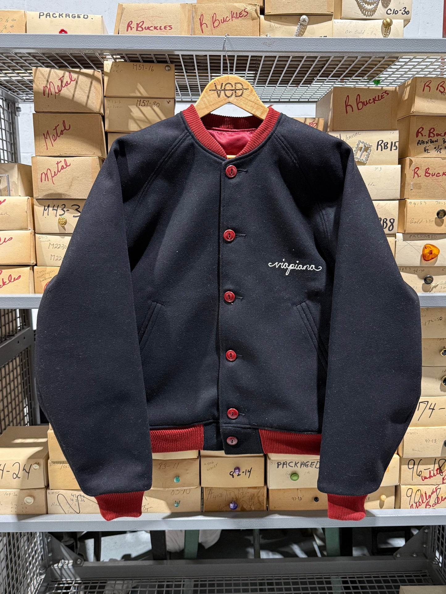 Black jacket with red accents on a hanger amidst stacked boxes in an indoor setting