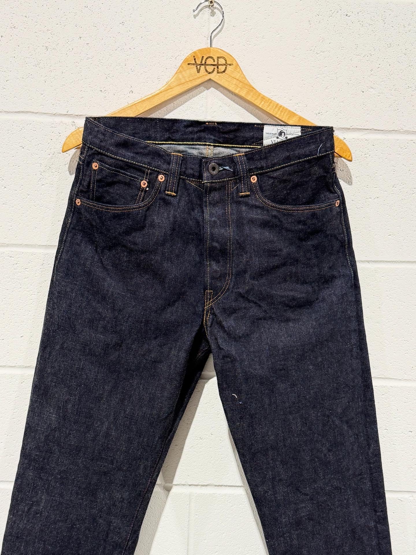 Pair of dark blue jeans on a wooden hanger against a white wall.