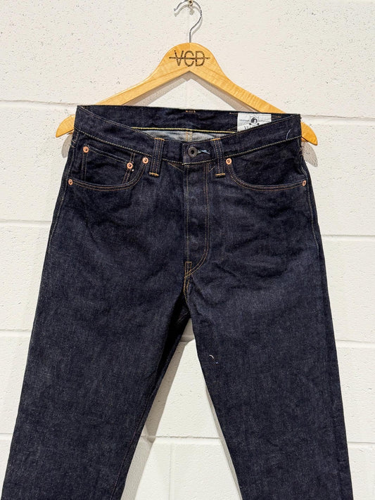 Pair of dark blue jeans on a wooden hanger against a white wall.