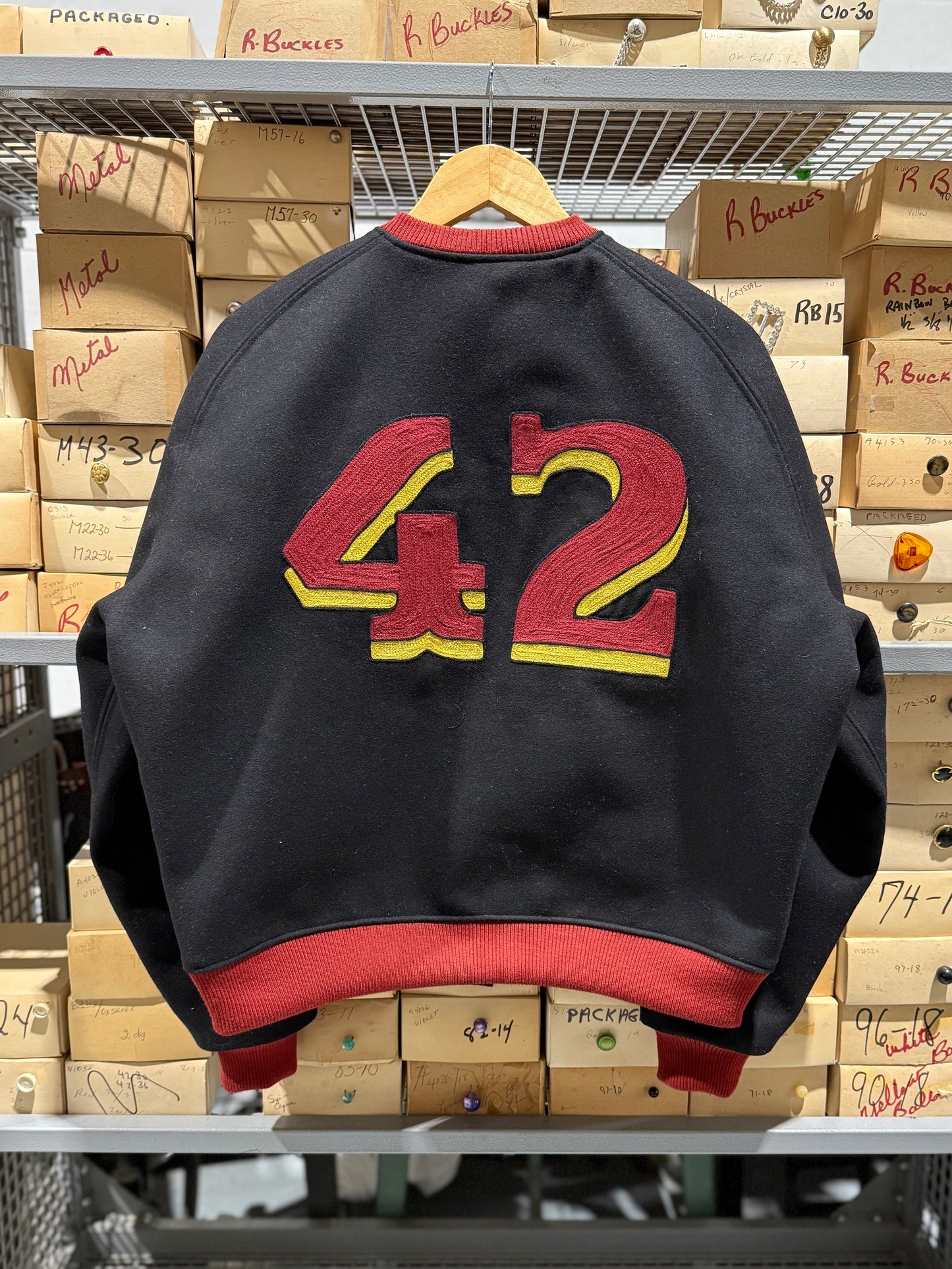 Black jacket with red and yellow number 42 on a rack with boxes in the background