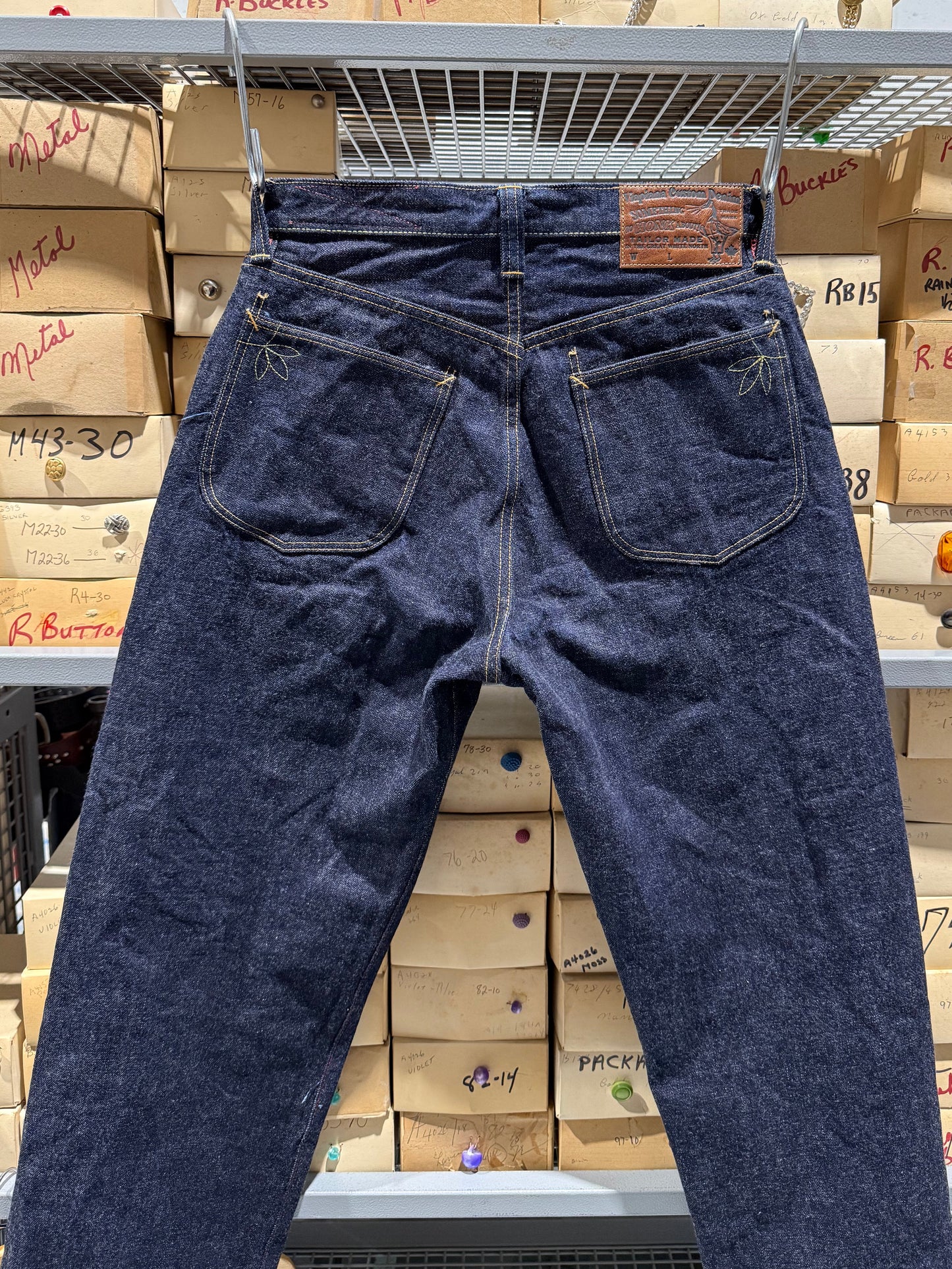 Crested jean hanging in front of boxes of buttons showing the details on the back. 