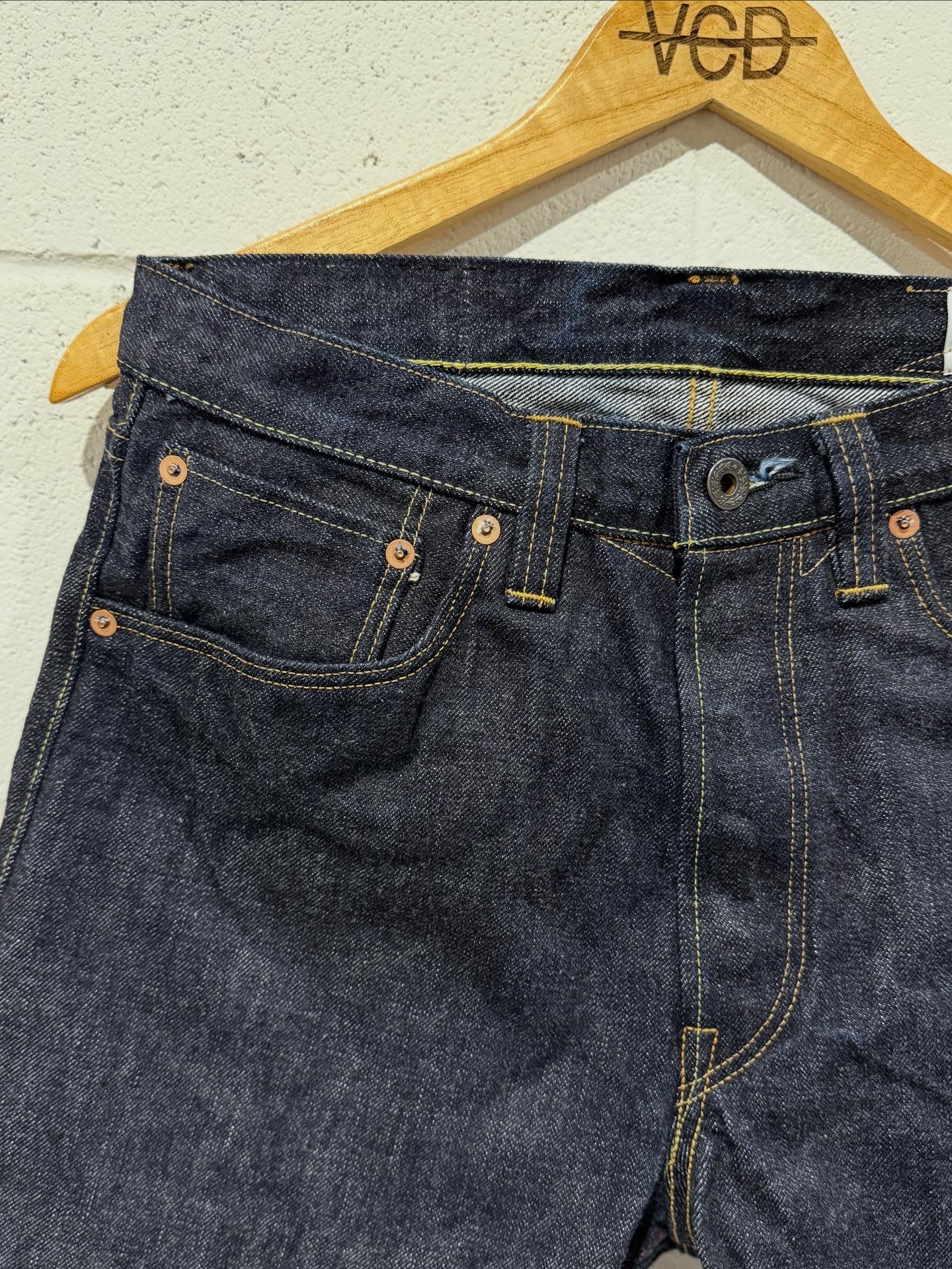 Pair of blue jeans on a wooden hanger against a white wall.