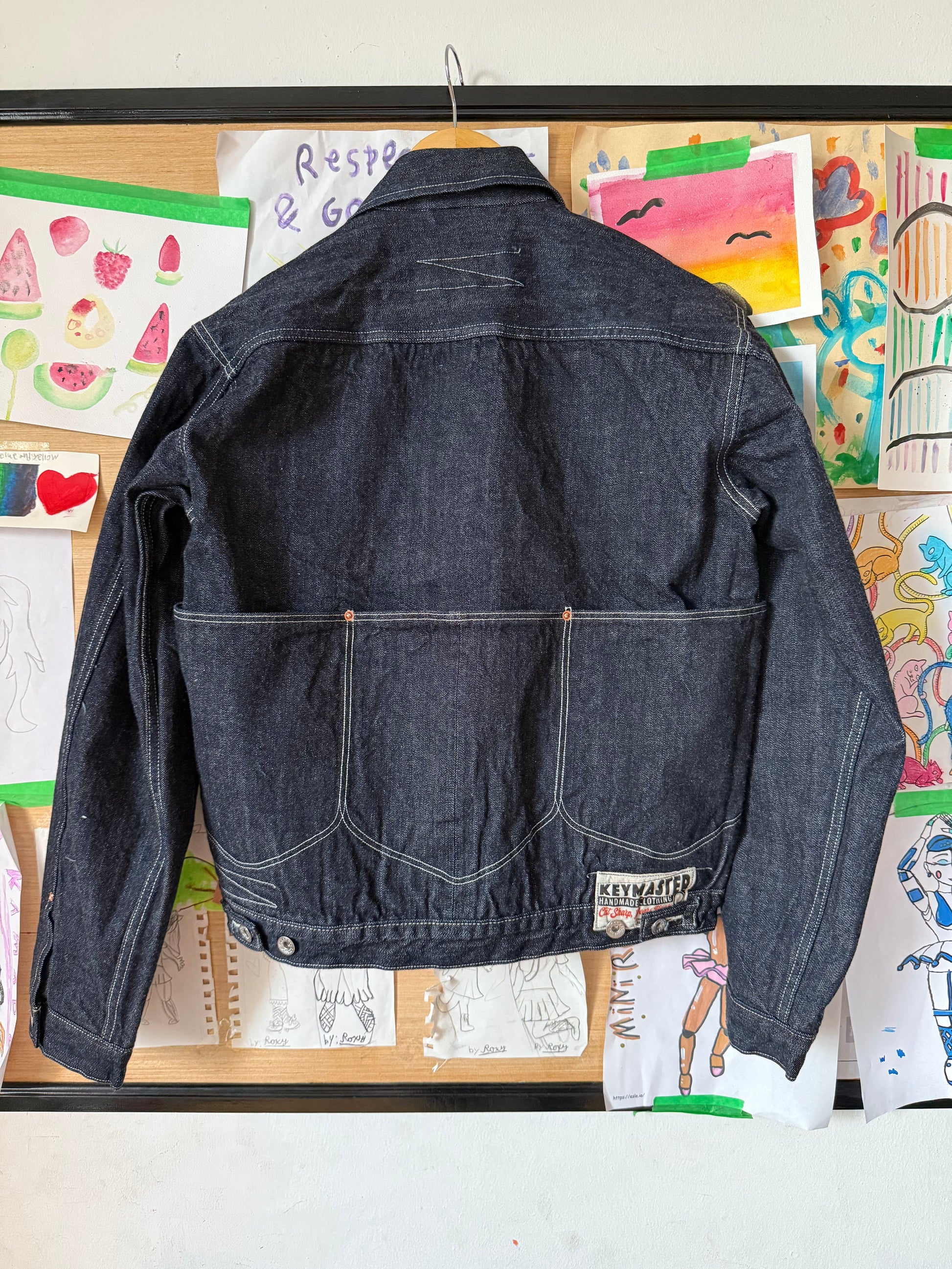 Indigo denim jacket on a surface with colorful children's drawings in the background