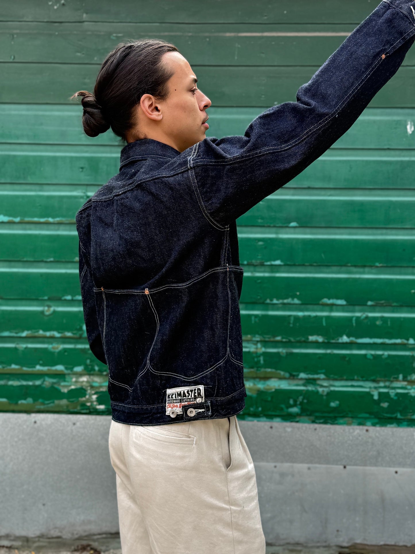 Elio wearing a dark denim jacket with a visible brand label against a green wall.
