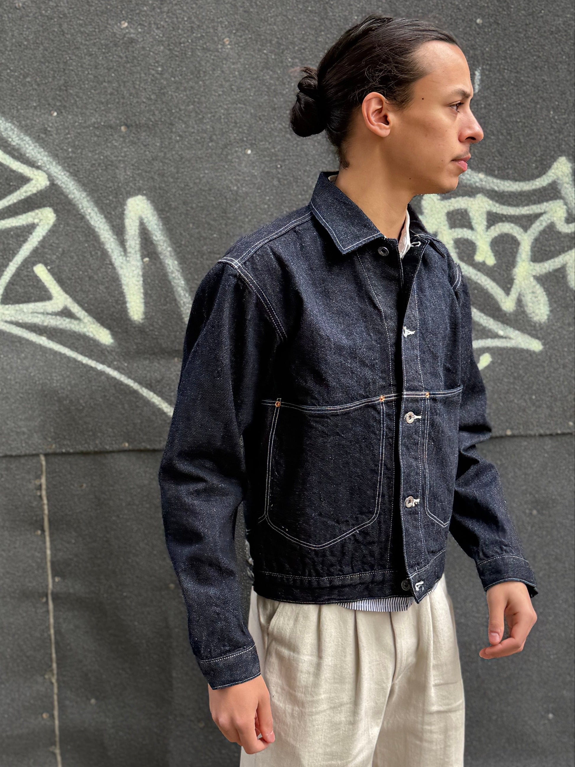 Elio wearing a dark denim jacket in front of a graffiti-covered wall